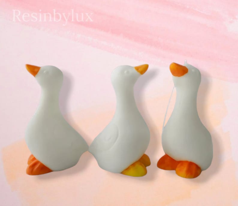 May include: Three white ceramic goose figurines with orange feet and beaks. The geese are facing different directions.
