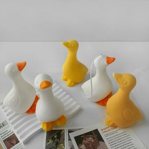 May include: Five small ceramic duck figurines in white and yellow. The ducks are arranged on a white surface with a striped pattern.