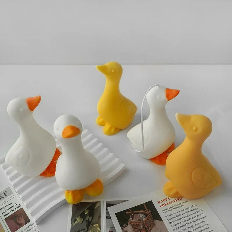 May include: Five small ceramic duck figurines in white and yellow. The ducks are arranged on a white surface with a striped pattern.