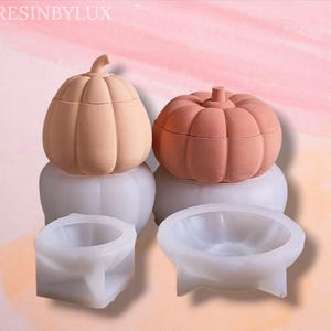 May include: Two pumpkin-shaped containers, one peach and one coral, sit atop white bases. Below are two white, pumpkin-shaped molds. The containers have lids and are designed to resemble pumpkins. The text "RESINBYLUX" is in the top left corner.
