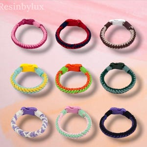 May include: Nine braided cord bracelets arranged in a grid, each featuring a plastic side-release buckle. The bracelets display various colour combinations including pink, red and navy, brown and tan, yellow and blue, orange and green, dark green, purple and white, light green and pink, and black and purple.