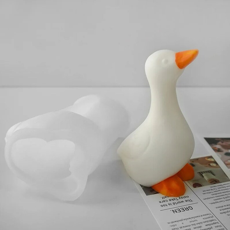 May include: White silicone mould shaped like a goose with an orange beak. The mould is sitting on a newspaper with the text "GREEN. The world is too noisy Take care"