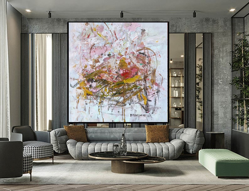 May include: Abstract painting with pink, white, and gold paint splatters and brushstrokes. The painting is framed and hanging on a wall in a modern living room.