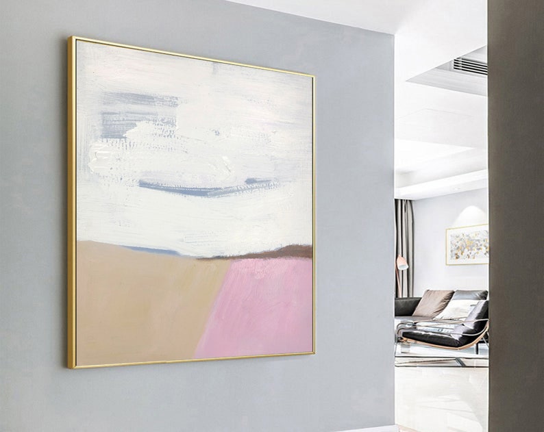 May include: Abstract painting with a gold frame. The painting features a white background with a light blue horizontal line and a brown and pink landscape at the bottom.