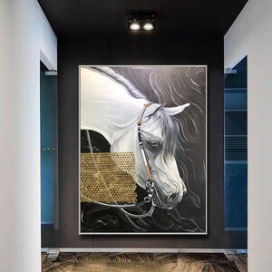 May include: A painting of a white horse with a gold bridle, set against a black background with gold accents. The horse's head is turned to the side, and its eye is visible. The painting is framed in a silver frame.