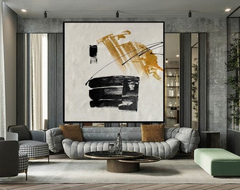 May include: Abstract painting with black and gold brushstrokes on a white canvas. The painting is hanging on a wall in a modern living room with a gray sofa and green ottoman.