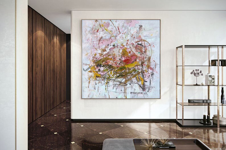 May include: Abstract painting with pink, white, and gold paint splatters and brushstrokes. The painting is framed and hanging on a white wall in a modern interior.