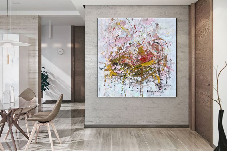 May include: Abstract painting with pink, white, and gold paint splatters and brushstrokes. The painting is framed and hanging on a wall in a modern home.