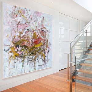 May include: Abstract painting with pink, white, and gold paint splatters and brushstrokes. The painting has a textured surface and is framed in a white frame.