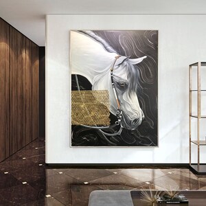 May include: A painting of a white horse's head with a black background. The horse has a golden bridle and is looking to the left. The painting is framed and hanging on a white wall.