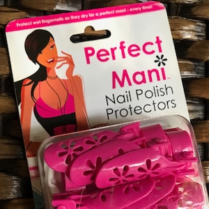 Puede incluir: Protectores de esmalte de uñas rosas en un paquete de plástico transparente con fondo blanco. El paquete tiene una ilustración rosa y blanca de una mujer con un collar rosa y una blusa rosa. El texto en el paquete dice "Perfect Mani Nail Polish Protectors".