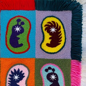 May include: A colorful rug with a geometric design featuring four bean-shaped figures with different colored backgrounds and fringe borders.