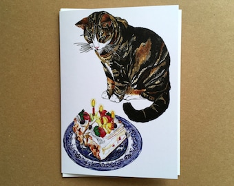 May include: A tabby cat looks at a birthday cake with lit candles on a blue and white plate. The cake is decorated with fruit and whipped cream.