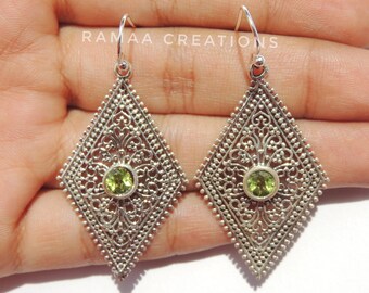 May include: A pair of silver filigree earrings with green gemstones. The earrings are in the shape of a diamond and have a delicate, intricate design.