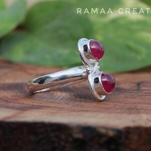 Pu&ograve; includere: Un anello d'argento con due pietre preziose rosse. L'anello &egrave; progettato con una fascia attorcigliata e le pietre preziose sono incastonate in una montatura a  bezel.