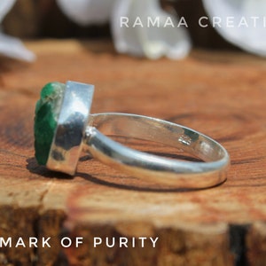 May include: A silver ring with a green gemstone set in a bezel setting. The ring is marked "925 - MARK OF PURITY" on the band.