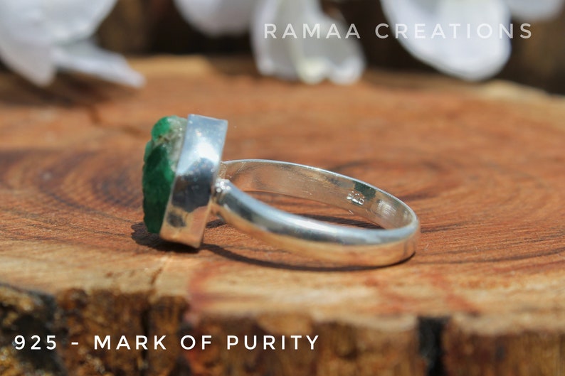 May include: A silver ring with a green gemstone set in a bezel setting. The ring is marked "925 - MARK OF PURITY" on the band.