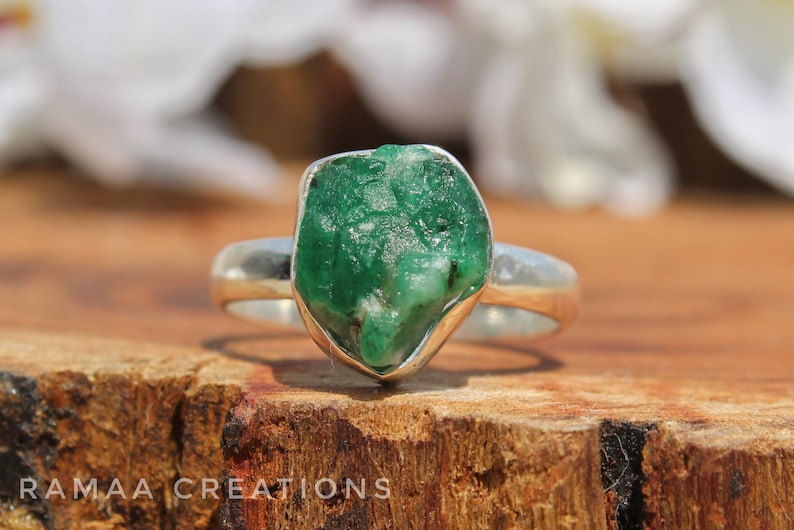 May include: A silver ring with a large, raw emerald gemstone. The emerald is a deep green color and has a rough, natural texture.