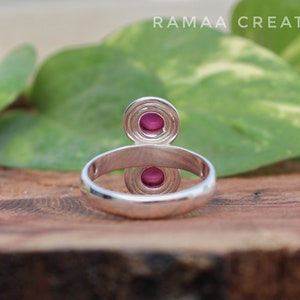 Pu&ograve; includere: Un anello d'argento con due pietre preziose rosa incastonate in un design circolare. L'anello &egrave; su una superficie di legno.