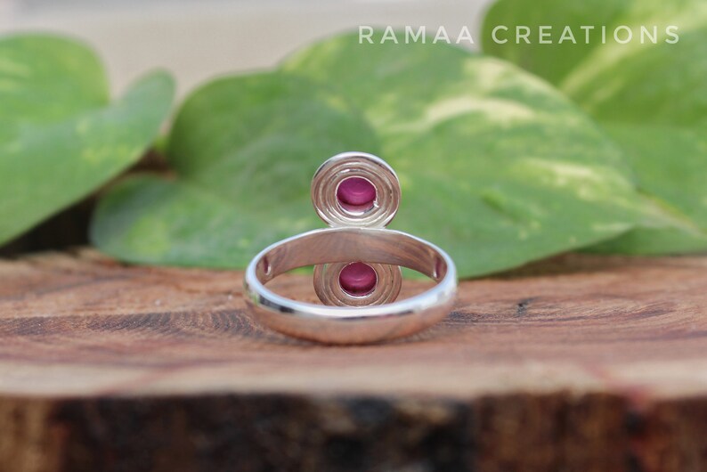 Pu&ograve; includere: Un anello d'argento con due pietre preziose rosa incastonate in un design circolare. L'anello &egrave; su una superficie di legno.