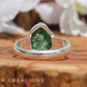 May include: A silver ring with a green gemstone set in the center. The gemstone is a rough cut and has a natural, organic shape.