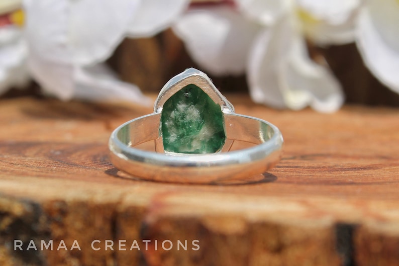 May include: A silver ring with a green gemstone set in the center. The gemstone is a rough cut and has a natural, organic shape.