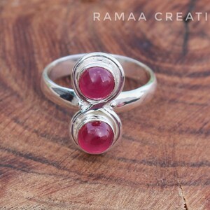 Pu&ograve; includere: Un anello d'argento con due pietre preziose rosa incastonate in un design unico a doppio anello.