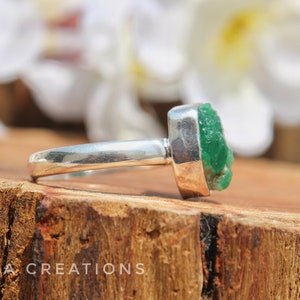 May include: A silver ring with a large, green, emerald-like gemstone. The gemstone is rough and has a natural, unpolished look.