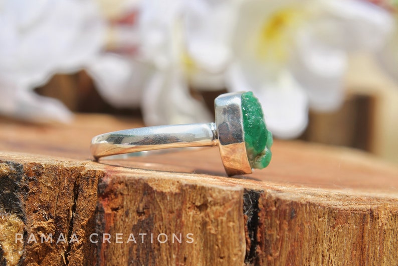 May include: A silver ring with a large, green, emerald-like gemstone. The gemstone is rough and has a natural, unpolished look.