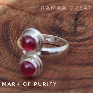 Pu&ograve; includere: Un anello d'argento con due pietre preziose rosa incastonate in un design a doppia fascia. L'anello &egrave; contrassegnato da "925 - MARK OF PURITY" e "925" sulla fascia interna.