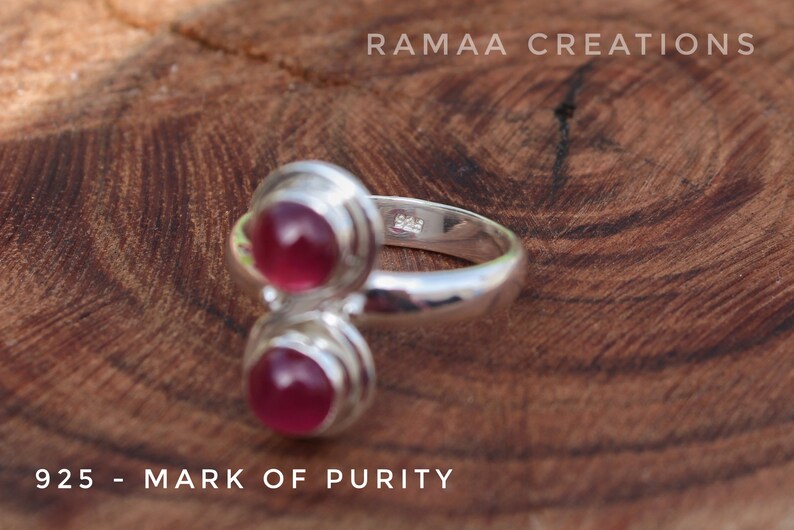 Pu&ograve; includere: Un anello d'argento con due pietre preziose rosa incastonate in un design a doppia fascia. L'anello &egrave; contrassegnato da "925 - MARK OF PURITY" e "925" sulla fascia interna.