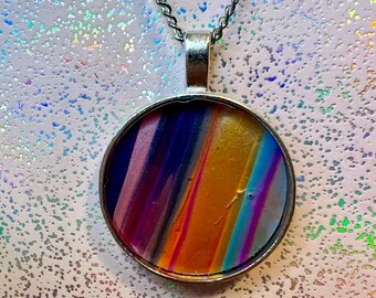 May include: A silver chain necklace with a round pendant featuring a colorful abstract design. The pendant has a silver rim and a clear glass cover.