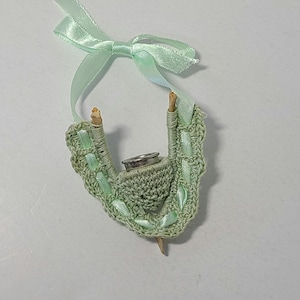 May include: A green crocheted thimble holder with a silver thimble inside. The holder is attached to a green ribbon with a bow.