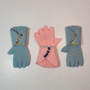 May include: Three felt mittens, one pink and two blue. The blue mittens have gold sequins and a blue button. The pink mitten has blue buttons.