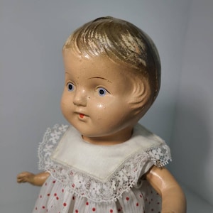 May include: A vintage porcelain doll with painted blue eyes and a white dress with red polka dots and lace trim.