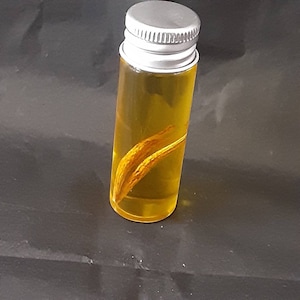 May include: A small glass bottle with a silver lid filled with a yellow liquid and containing a dried, light brown plant material.