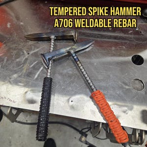 Puede incluir: Dos martillos de punta templada hechos de varilla corrugada soldable A706. Un martillo tiene un mango envuelto en cordón negro, mientras que el otro tiene un mango envuelto en cordón naranja. El texto TEMPERED SPIKE HAMMER A706 WELDABLE REBAR es visible.