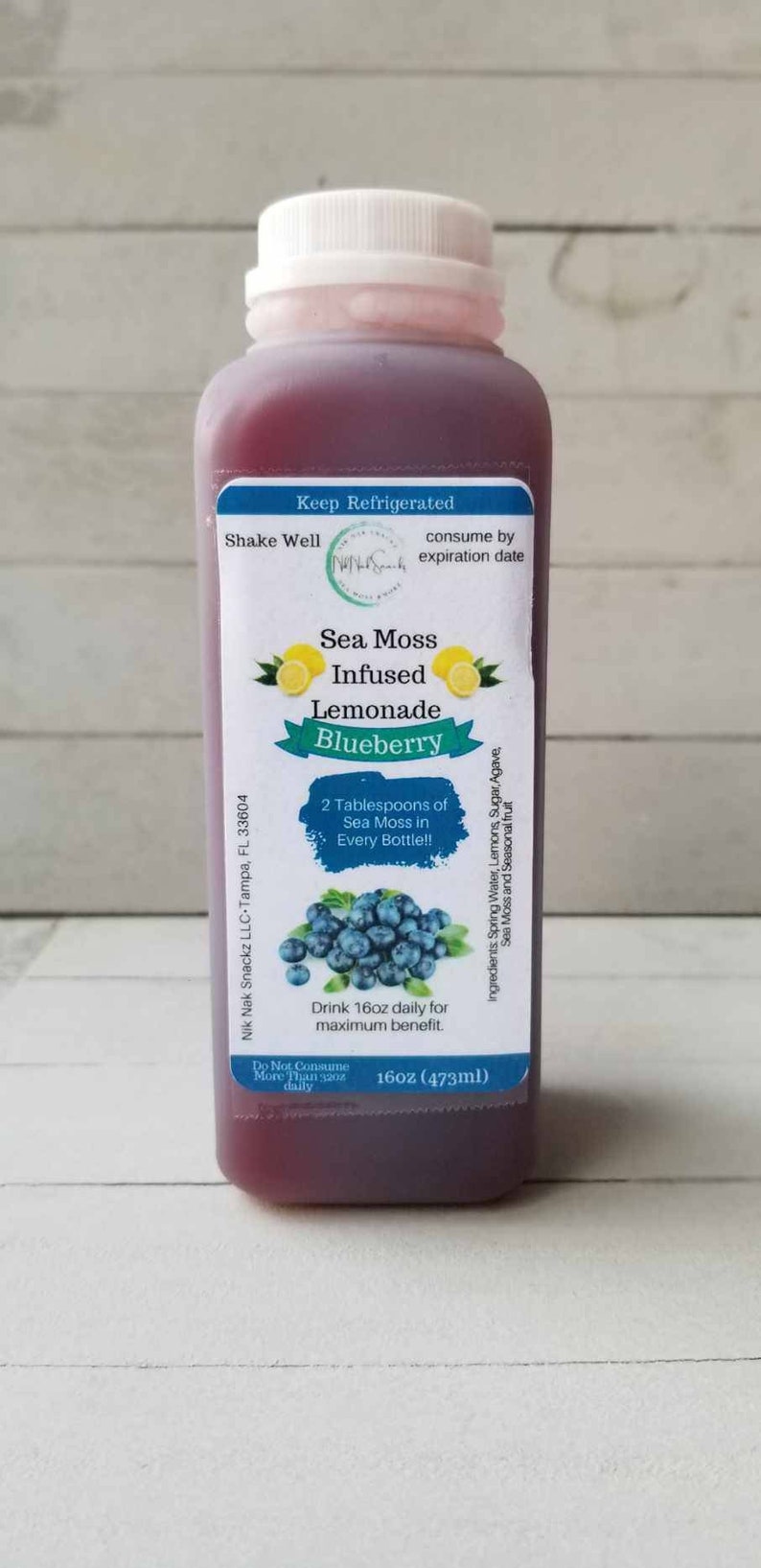 May include: A 473ml bottle of blueberry sea moss infused lemonade. The bottle has a blue label with the words "Sea Moss Infused Lemonade Blueberry" and "2 Tablespoons of Sea Moss in Every Bottle!!".