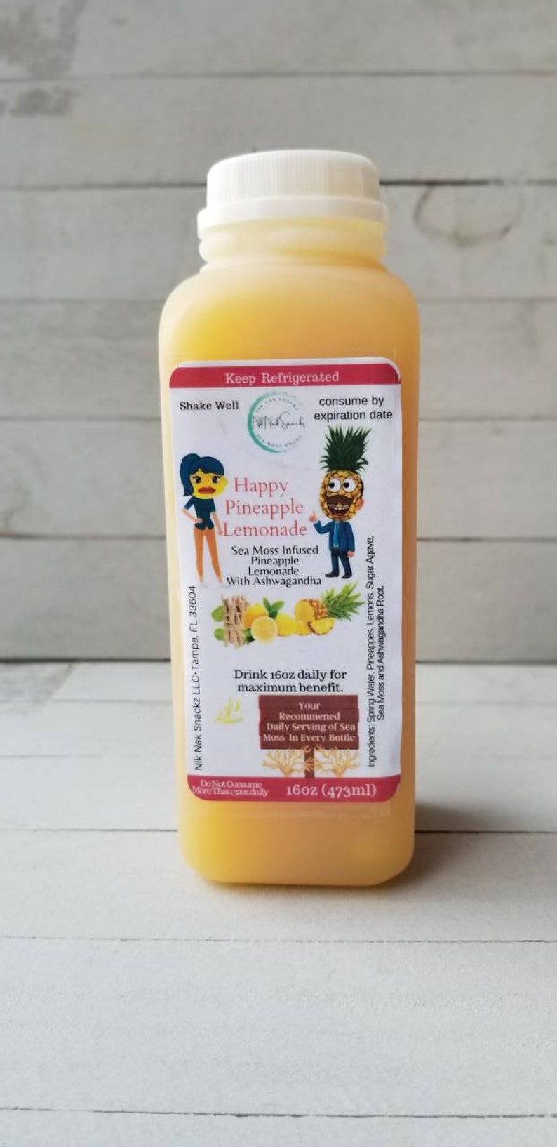 May include: A 473ml bottle of Happy Pineapple Lemonade with a yellow label featuring a cartoon pineapple and a woman. The label reads "Sea Moss Infused Pineapple Lemonade with Ashwagandha".