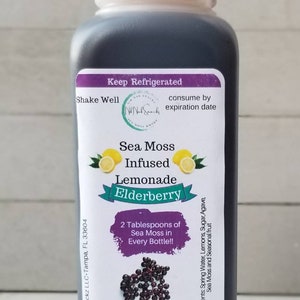 May include: A clear glass bottle with a white lid filled with a dark liquid. The label reads "Sea Moss Infused Lemonade Elderberry" and includes instructions to "Keep Refrigerated" and "Shake Well". The label also states that the product contains 2 tablespoons of sea moss per bottle and that the recommended daily serving is 16 ounces.