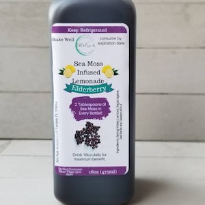 May include: A 473ml bottle of Sea Moss Infused Lemonade with Elderberry. The bottle is dark brown and has a white label with the product name, ingredients, and instructions. The label also features a picture of lemons and elderberries.
