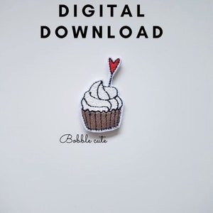 Op de afbeelding: Geborduurde cupcake-patch met witte glazuur, een bruine basis en een rood hart. De woorden "DIGITAL DOWNLOAD" staan boven de cupcake en "Bobble cute" eronder.