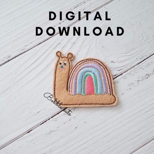May include: A tan felt snail applique with a rainbow shell. The rainbow features pastel colors of pink, blue, and purple. The text "DIGITAL DOWNLOAD" is above the snail, and the text "Bobble cute" is below the snail.