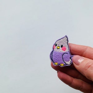 Può includere: Toppa ricamata viola di un piccolo uccello con guance rosa, da stirare.