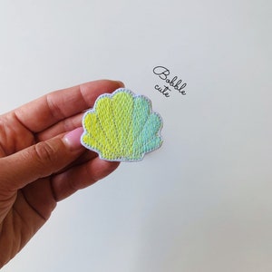 May include: A yellow and blue seashell embroidered patch with white stitching. The patch is on a white background.