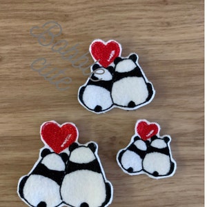 May include: Three panda bear patches with a red heart. The pandas are black and white with a heart above them. The patches are on a wooden surface. The text "Barbie cute" is in the upper left corner.