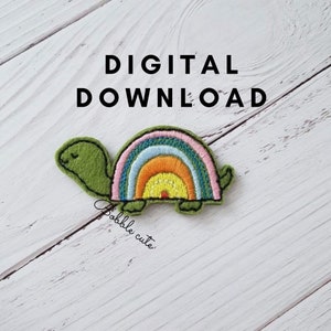 Könnte beinhalten: Ein grüner, schildkrötenförmiger Aufnäher mit einem Regenbogenmuster auf dem Panzer. Der Aufnäher hat einen gestickten Rand und den Text "DIGITAL DOWNLOAD" in Schwarz. Der Aufnäher befindet sich auf einer weißen Holzoberfläche.