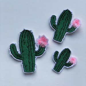 May include: Three embroidered cactus patches with pink flowers. The patches are on a white background.