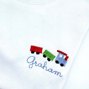 May include: White t-shirt with a blue, green, and red embroidered train and the name "Graham" underneath.