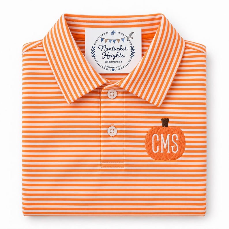 May include: An orange and white striped polo shirt featuring a collar and a three-button placket. An embroidered orange pumpkin with the white monogram letters CMS is on the chest. A white tag reads Nantucket Heights Embroidery Established 2019.